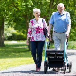 Two people walking outdoors, one using a Rollator Wheelchair.