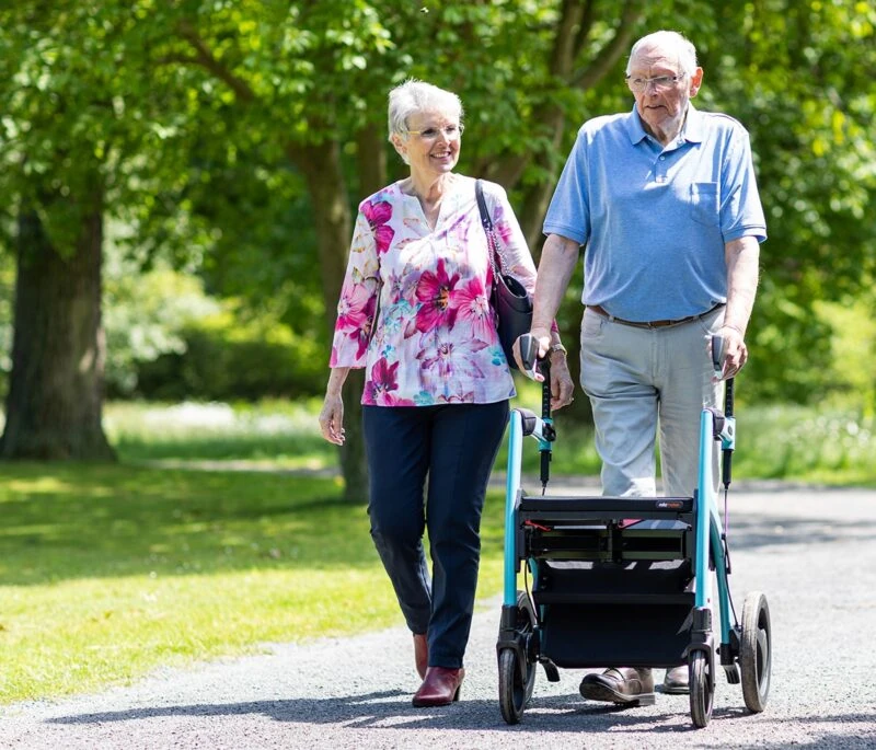 Two people walking outdoors, one using a Rollator Wheelchair.