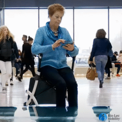 Person seated on a Rollz Flex Shopper rollator in a busy indoor area.