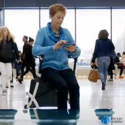 Person seated on a Rollz Flex Shopper rollator in a busy indoor area.