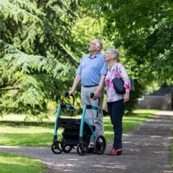 Two people walking with a Rollator Wheelchair on a tree-lined path.