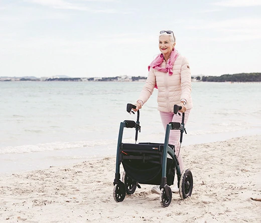 Person using Rollz Motion Rhythm Rollator on a sandy beach.