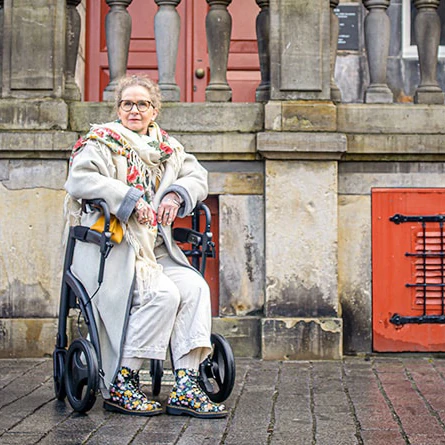 Person seated on a Rollz Motion Rhythm Rollator in an outdoor setting.