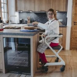 Person seated on Saljol Indoor Rollator with a wooden seat in a kitchen.