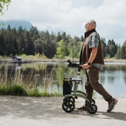 Man walking with a rollator near a scenic lake and forest.
