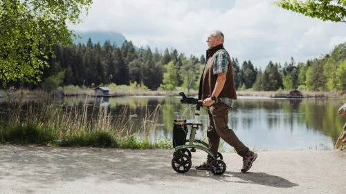Man walking with a rollator near a scenic lake and forest.