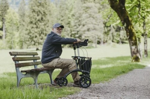 Man sitting on a bench with a Saljol Allround Crossover Rollator beside him.