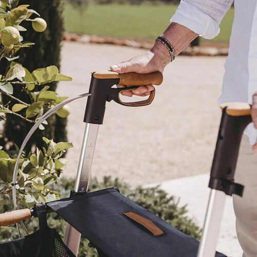 Person holding the handle of a Saljol Allround Crossover Rollator with cork armrests outdoors.