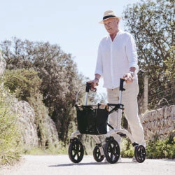 Person using the Saljol Allround Crossover Rollator on a sunny outdoor path.