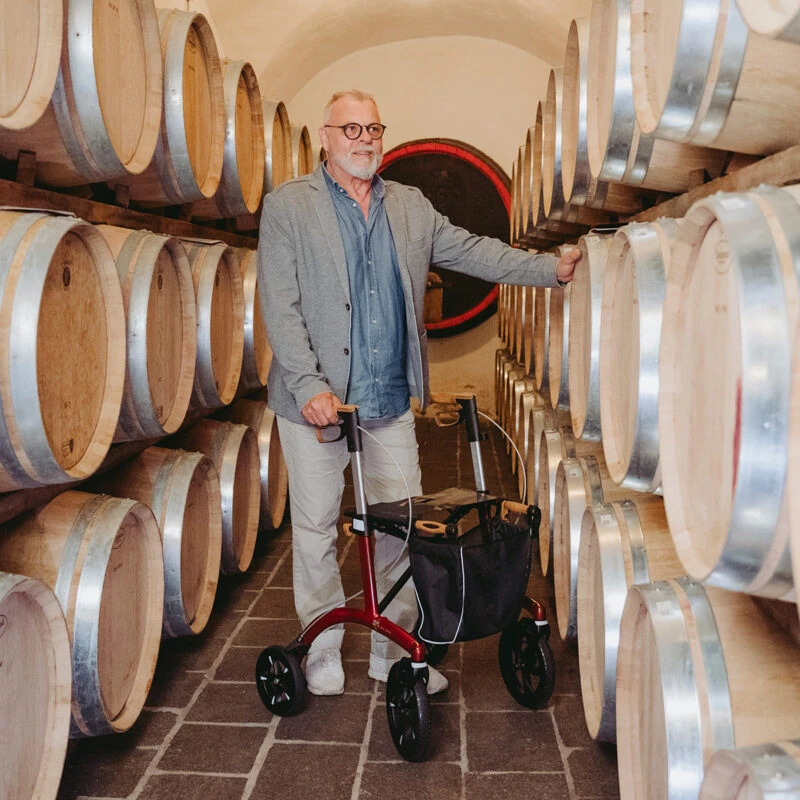Man using a red rollator in a wine cellar with wooden barrels.