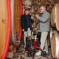 Two men in a wine cellar with a red Saljol Allround Crossover Rollator.