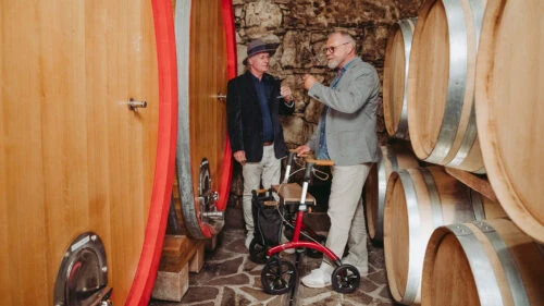 Two men in a wine cellar with a red Saljol Allround Crossover Rollator.