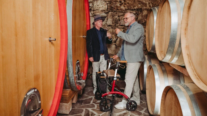 Two men in a wine cellar with a red Saljol Allround Crossover Rollator.