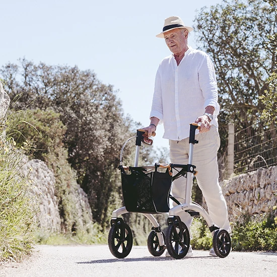 Person using the Saljol Allround Crossover Rollator on a sunny outdoor path.