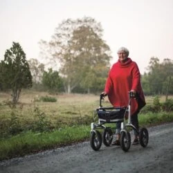 Person using Trionic Walker Rollator on a gravel path outdoors.