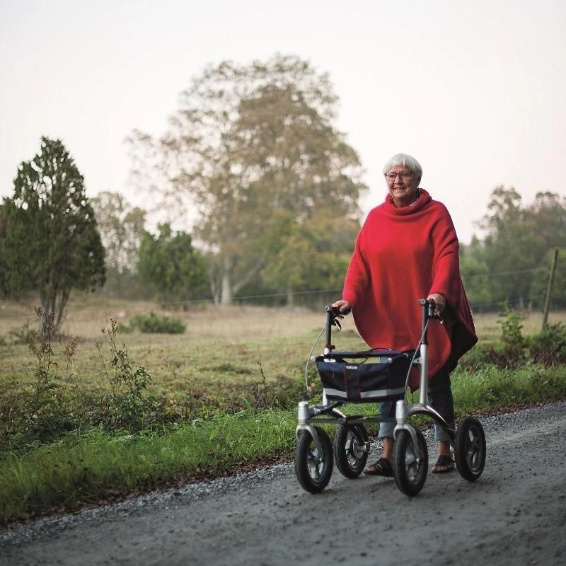 Person using Trionic Walker Rollator on a gravel path outdoors.