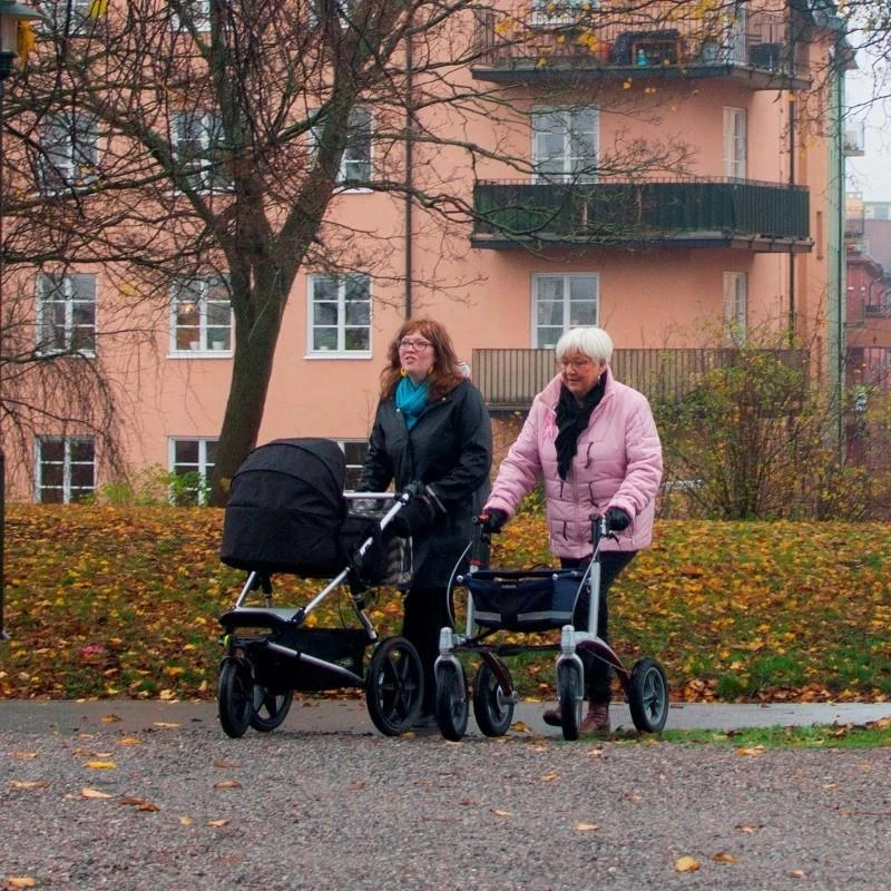 Two people walking with rollators on a path with autumn leaves.