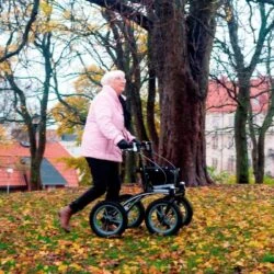 Person using Trionic 14er Rollator Walker on grassy terrain with fallen leaves.