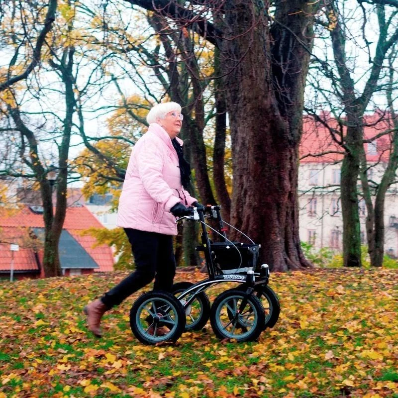 Person using Trionic 14er Rollator Walker on grassy terrain with fallen leaves.