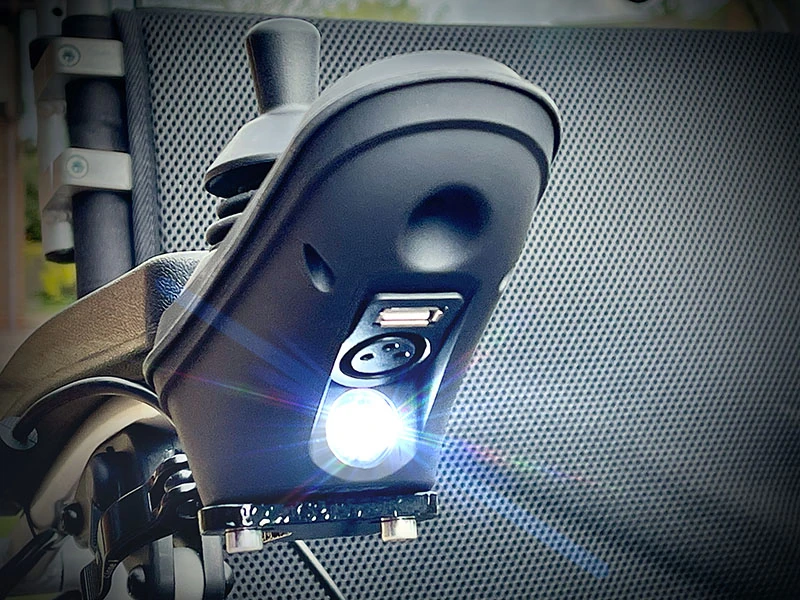 Close-up of a joystick with USB port and LED light on a wheelchair.