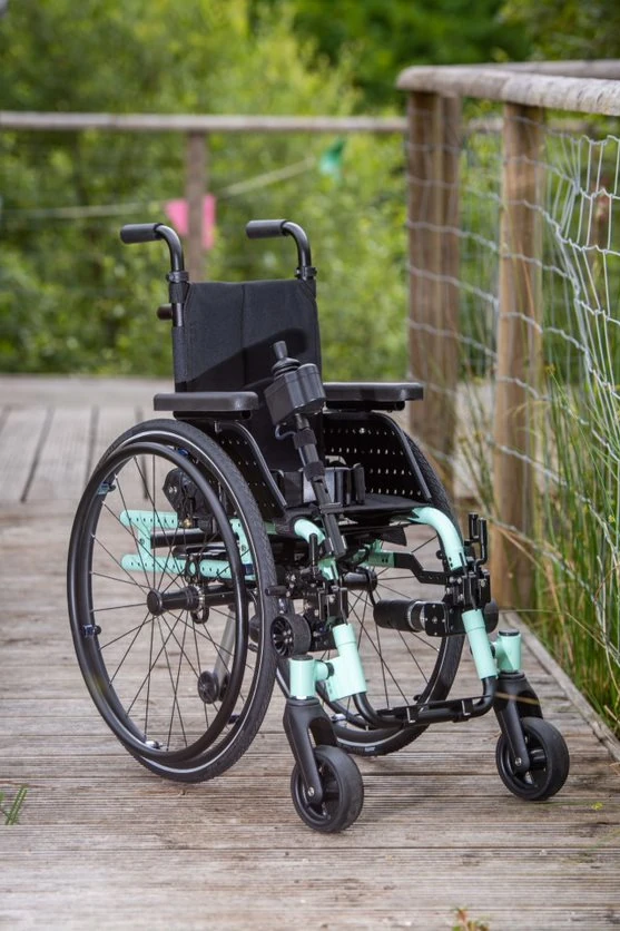 Compact electric wheelchair with mint green accents on a wooden path.