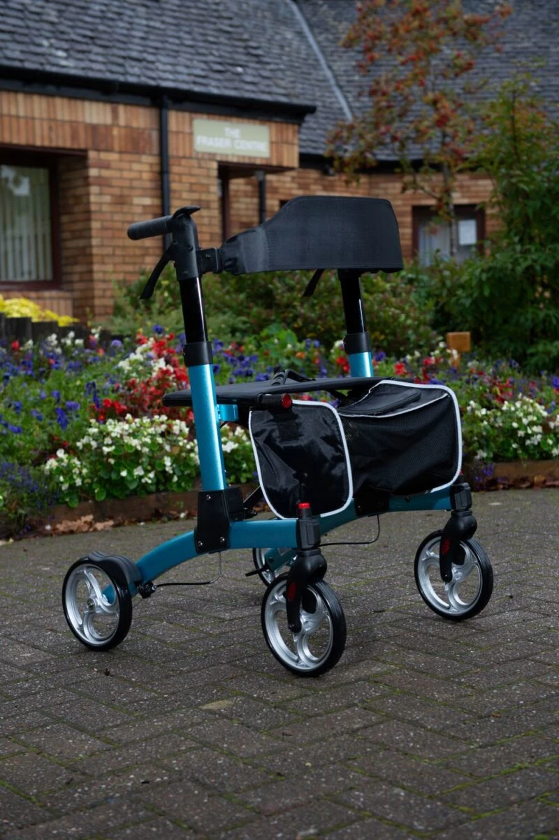 Blue folding rollator with seat and shopping bag in a garden setting.