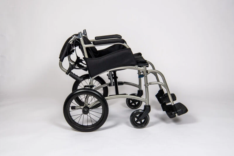 Side view of a folded lightweight transit wheelchair with black seat and silver frame.