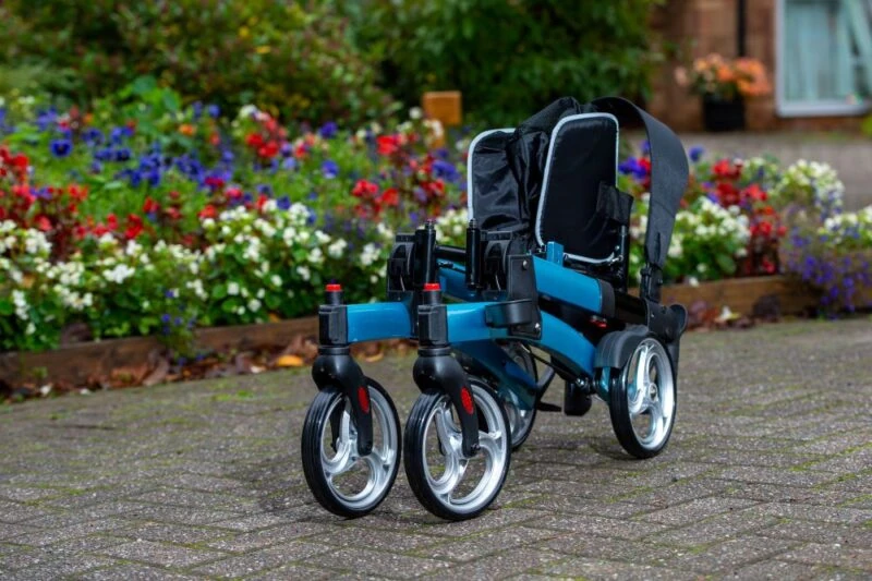 Folded blue rollator with large wheels on a paved path in a garden.