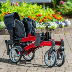 Red rollator folded on a paved path with flowers in the background.