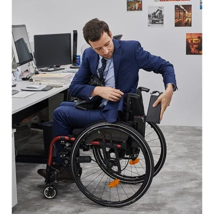 Person in a suit sitting in a compact power wheelchair at an office desk.