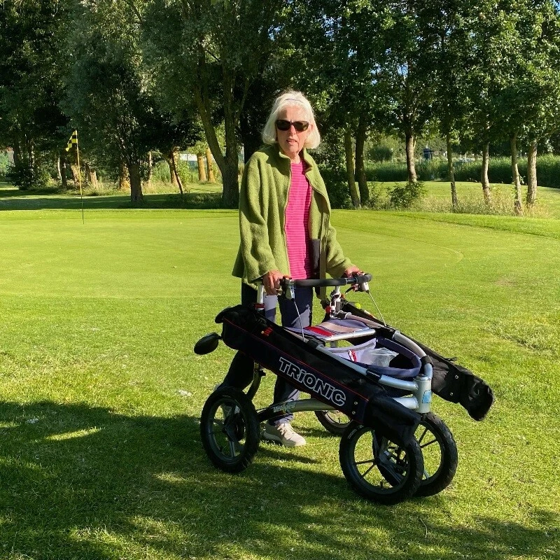 Person using a Trionic Veloped Golf Rollator on a golf course.
