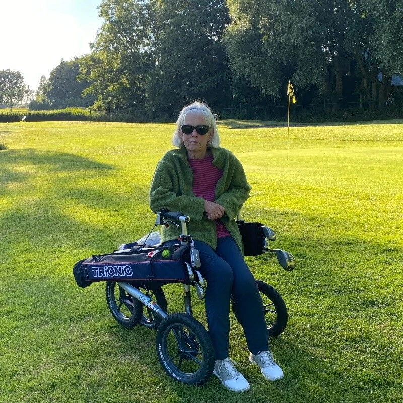 Person seated on a Veloped Golf 14er rollator on a golf course.