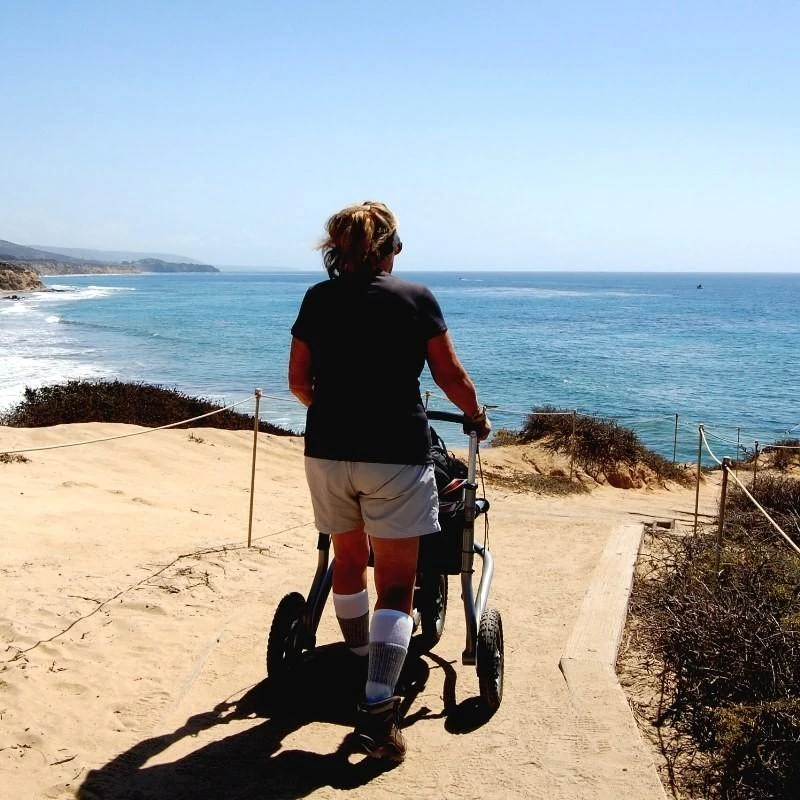 Person using Trionic Veloped Trek 12er on a sandy coastal path.