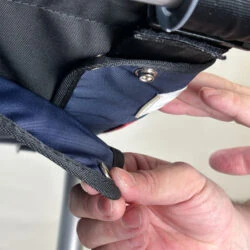 Close-up of hands adjusting a button on a fabric bag attached to a rollator.