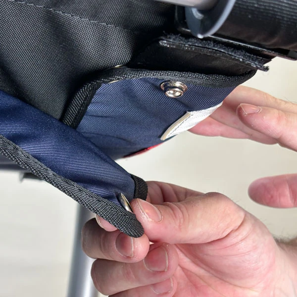 Close-up of hands adjusting a button on a fabric bag attached to a rollator.