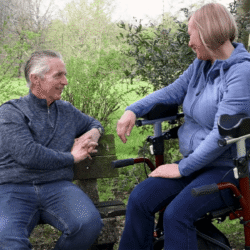 Two people sitting, one using a MobiWalk Upright Walker with pneumatic wheels.