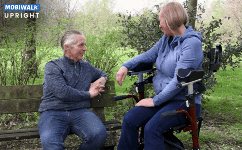 Two people sitting, one using a MobiWalk Upright Walker with pneumatic wheels.