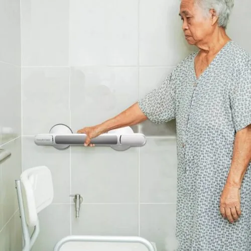 Elderly person holding a suction grab shower handle in a bathroom.