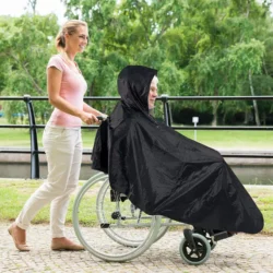 Person in wheelchair wearing a black waterproof poncho with hood outdoors.