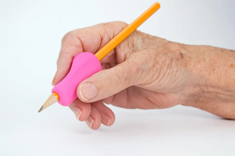 Elderly hand holding a pencil with a pink grip.