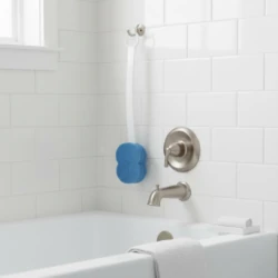 Blue sponge with long handle hanging in a white tiled bathroom.