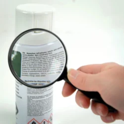 Hand holding a magnifier over a spray can label.