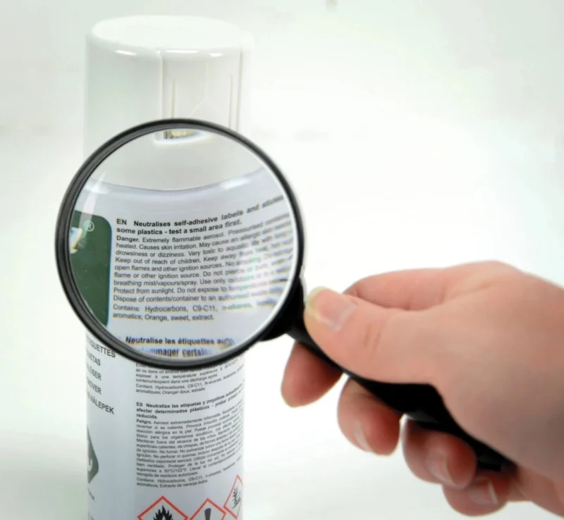 Hand holding a magnifier over a spray can label.