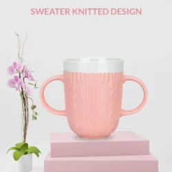 Pink two handled mug with a sweater knitted design on a pink platform.