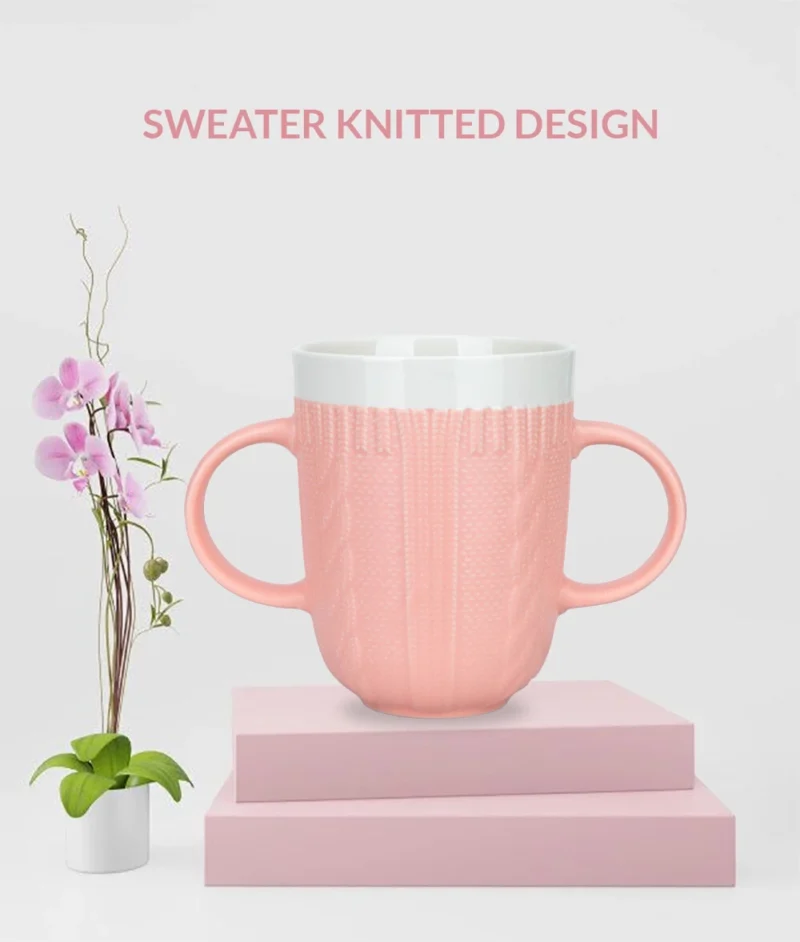 Pink two handled mug with a sweater knitted design on a pink platform.