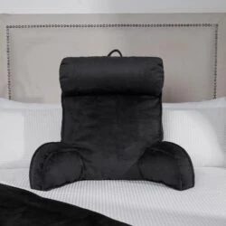 Black lumbar support pillow on a bed with a white textured blanket.