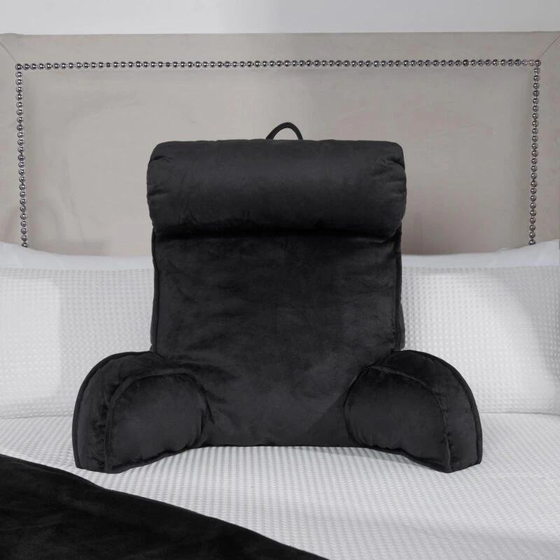 Black lumbar support pillow on a bed with a white textured blanket.
