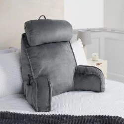 Grey lumbar support pillow with armrests on a bed.