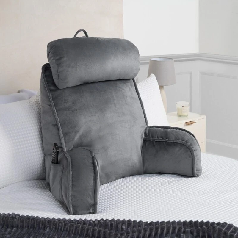 Grey lumbar support pillow with armrests on a bed.