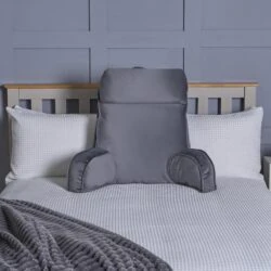 Grey lumbar support pillow on a bed with white pillows and a grey blanket.